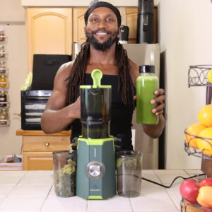 Person holding a green juice beside the LinkChef Cold Press Juicer on a kitchen counter